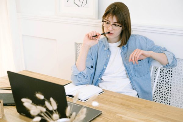 femme qui réfléchit devant son ordinateur, crayon à la bouche